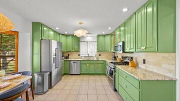 Una cocina con armarios verdes, electrodomésticos de acero inoxidable y piso de baldosas.
