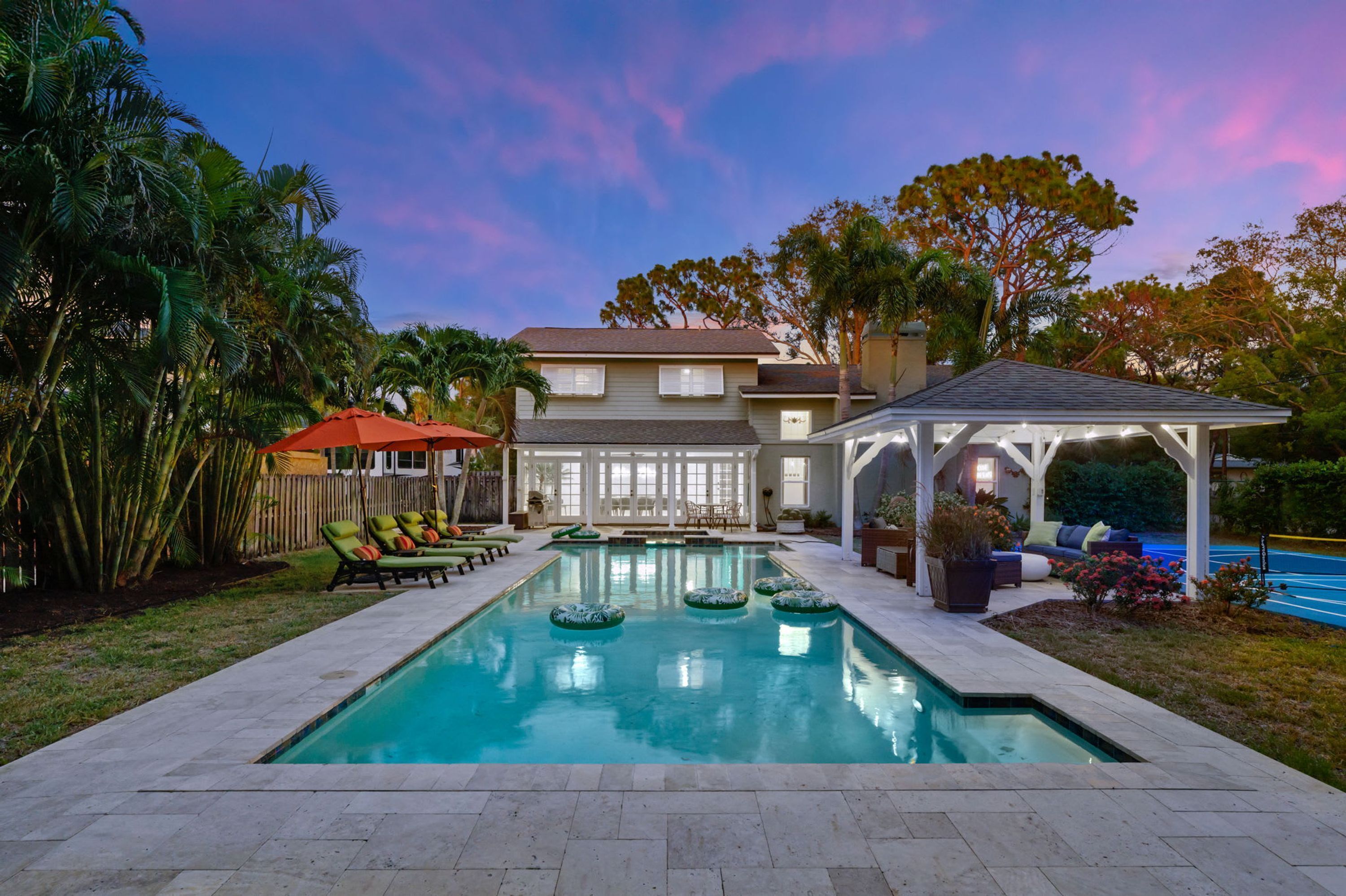 A backyard with a swimming pool, lounge chairs, and a covered patio area.