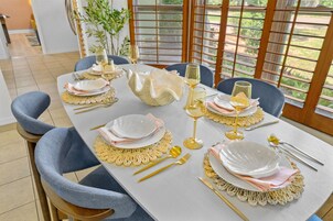 Mesa lista con platos, cubiertos y vasos, mostrando vistas de follaje por una ventana.