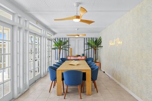 Un comedor con una mesa de madera y sillas azules, un ventilador de techo y un letrero de neón en la pared.