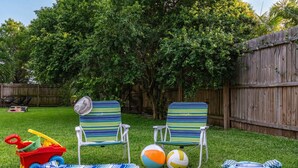 A backyard with two striped lawn chairs, a volleyball, a beach ball, and a blue shark-shaped pillow. - Kokomo House Pool Hot Tub Outdoor Games (Bradenton)