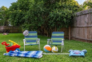 A backyard with two striped lawn chairs, a volleyball, a beach ball, and a blue shark-shaped pillow. - Kokomo House Pool Hot Tub Outdoor Games (Bradenton)