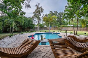 Un patio trasero con piscina, tumbonas de madera y valla de madera.