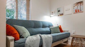 A modern living room with a blue sofa, orange and green cushions, a grey throw blanket, and a small round table. - Kokomo House Pool Hot Tub Outdoor Games (Bradenton)