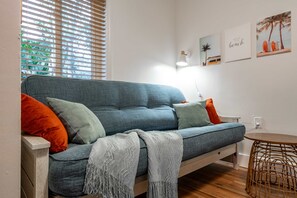 A modern living room with a blue sofa, orange and green cushions, a grey throw blanket, and a small round table. - Kokomo House Pool Hot Tub Outdoor Games (Bradenton)