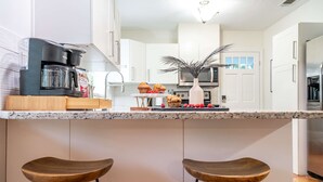 A modern kitchen with white cabinets, a coffee maker, a microwave, and two wooden bar stools. - Kokomo House Pool Hot Tub Outdoor Games (Bradenton)