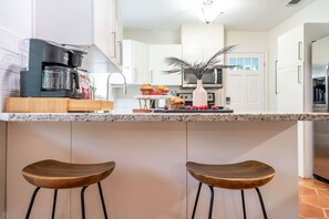 A modern kitchen with white cabinets, a coffee maker, a microwave, and two wooden bar stools. - Kokomo House Pool Hot Tub Outdoor Games (Bradenton)