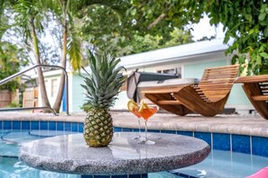 Escena junto a la piscina, con una piña y un cóctel sobre una mesa.