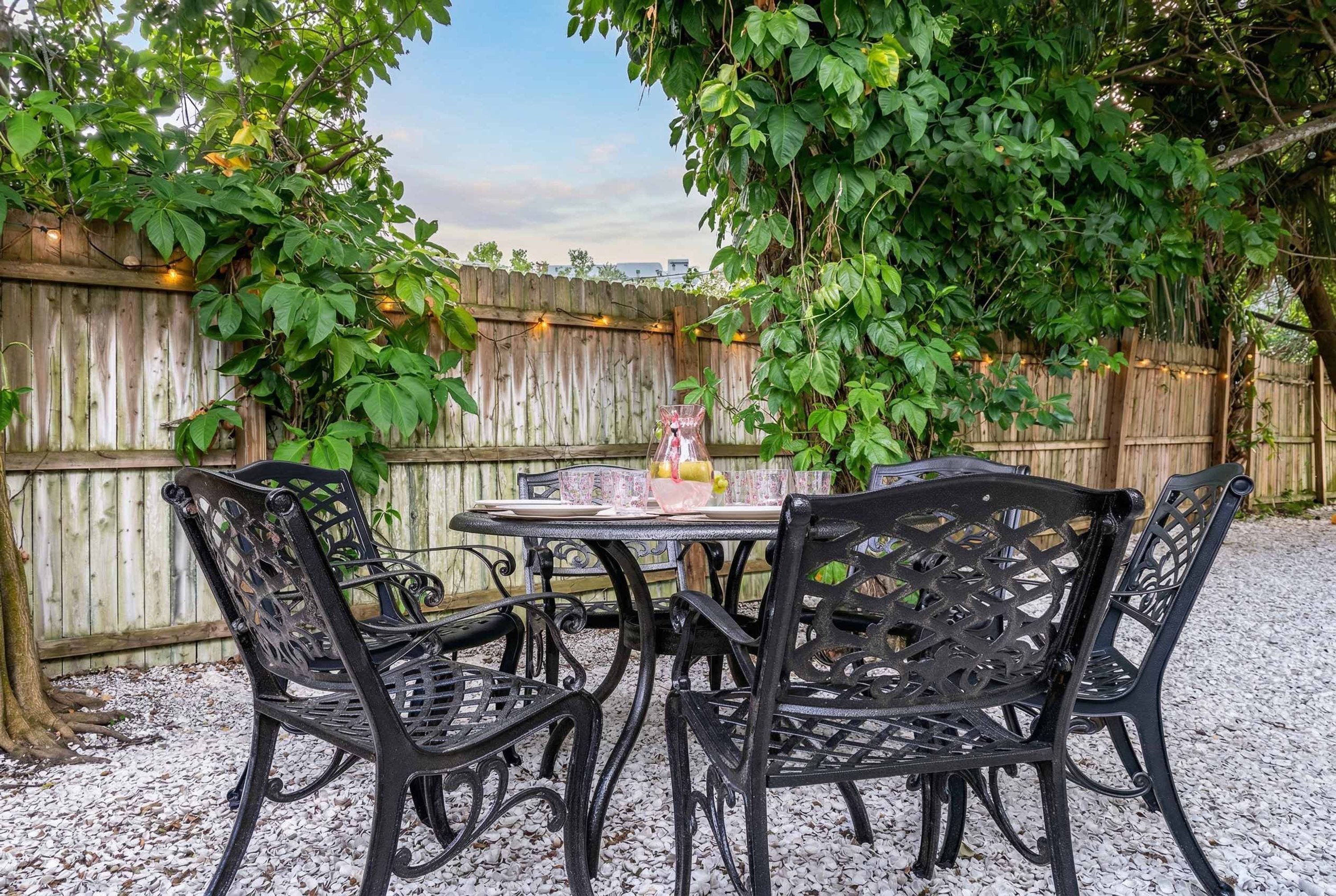 A patio with a round table and four chairs, surrounded by a wooden fence and greenery.