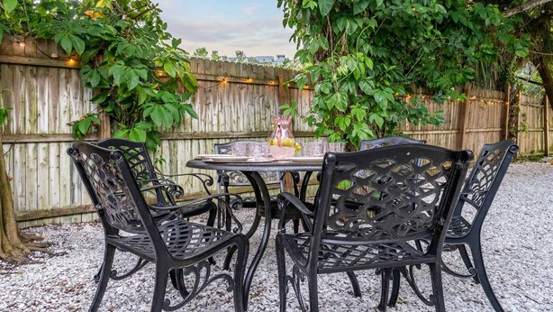 A patio with a round table and four chairs, surrounded by a wooden fence and greenery. - Kokomo House Pool Hot Tub Outdoor Games (Bradenton)