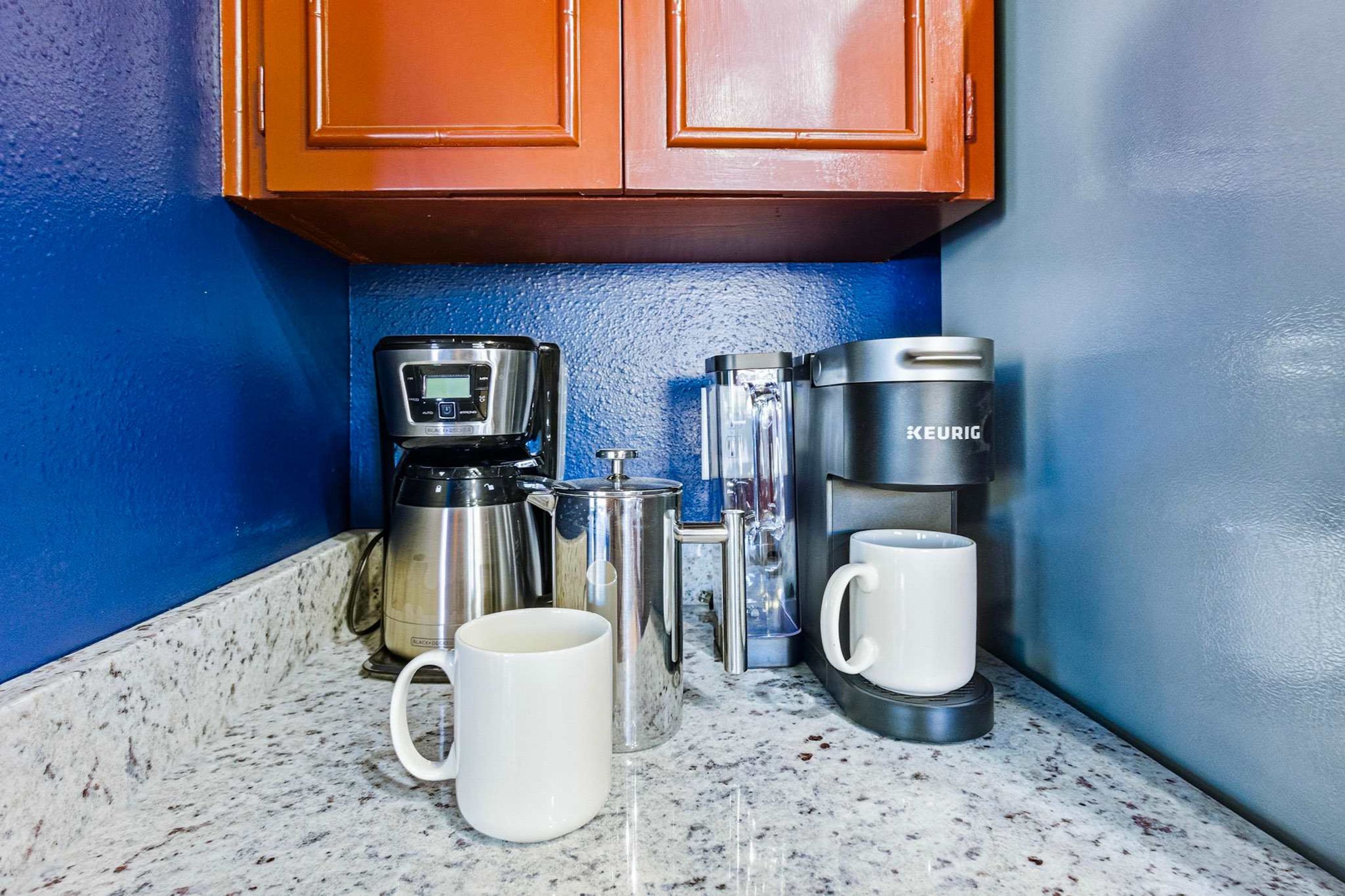 Una encimera de cocina con una cafetera, un hervidor, una taza y una jarra de café.