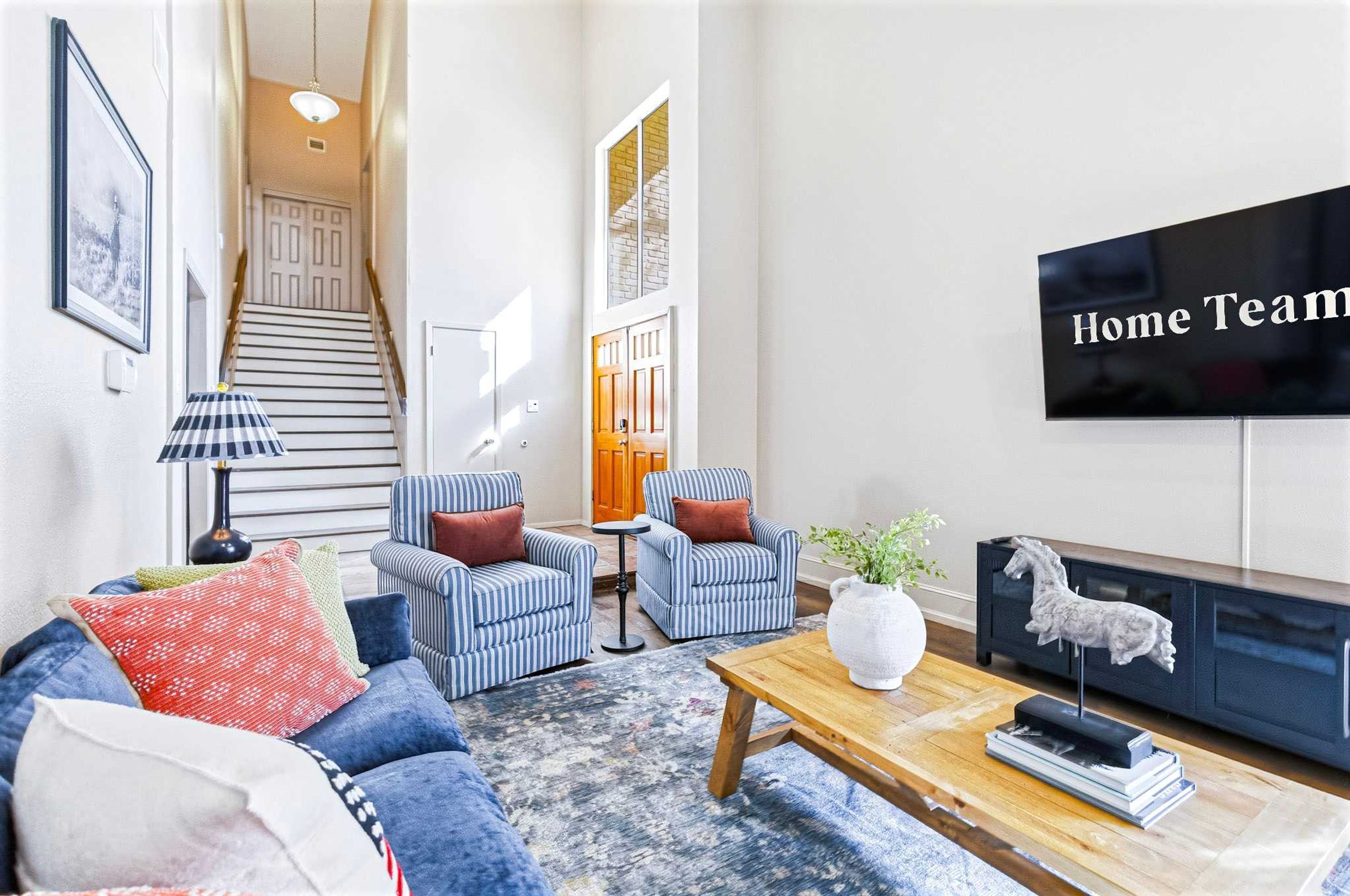 Un salon comprenant un canapé, deux fauteuils, une table basse, un téléviseur et un escalier.