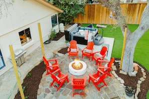 Eine Hinterhof-Terrasse mit Feuerstelle, Gartenmöbeln und Whirlpool.