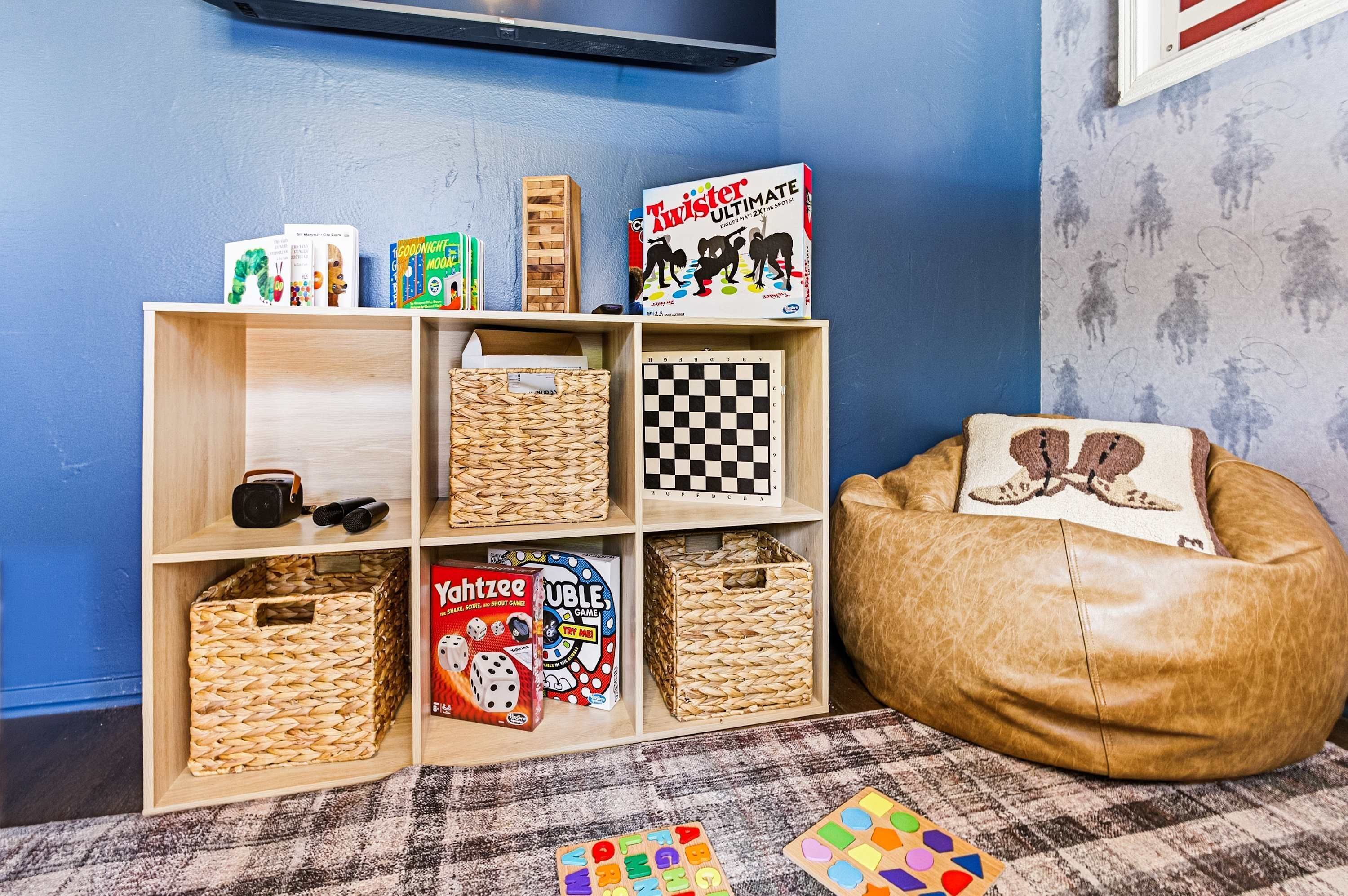 A room with a blue wall, a wooden bookshelf, a brown bean bag, and a checkered board game.