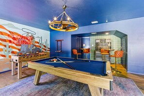 A pool table with a blue felt surface, surrounded by orange chairs, in a room with a blue wall and a mural. - Cowboy Ridge 4BR Spacious Retreat Sleeps 13 (San Antonio)