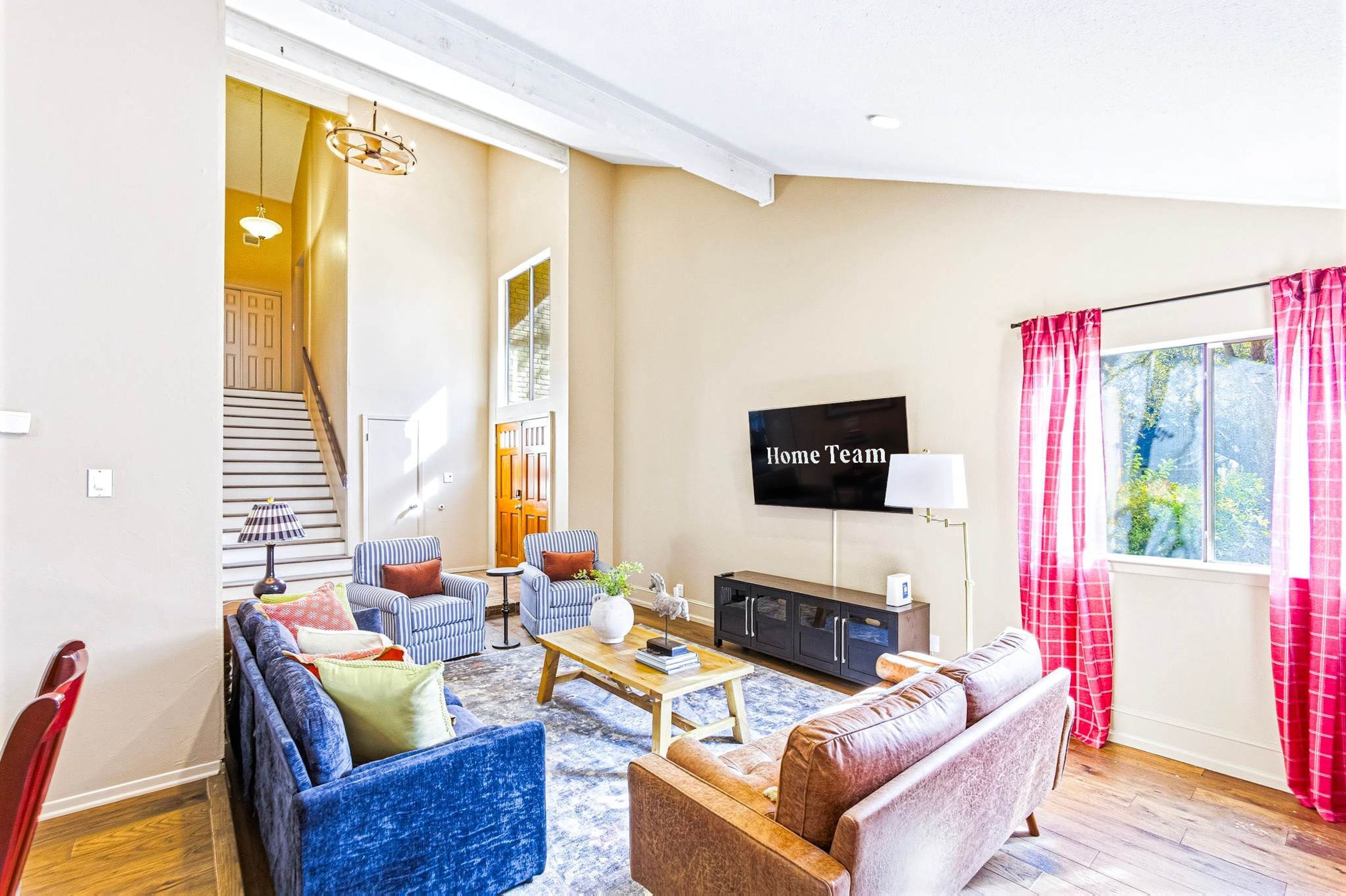 A living room with a sofa, armchairs, a coffee table, a TV, and a staircase leading to another room.