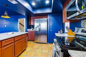 A kitchen with blue walls, a stainless steel refrigerator, a stove, and a microwave. - Cowboy Ridge 4BR Spacious Retreat Sleeps 13 (San Antonio)