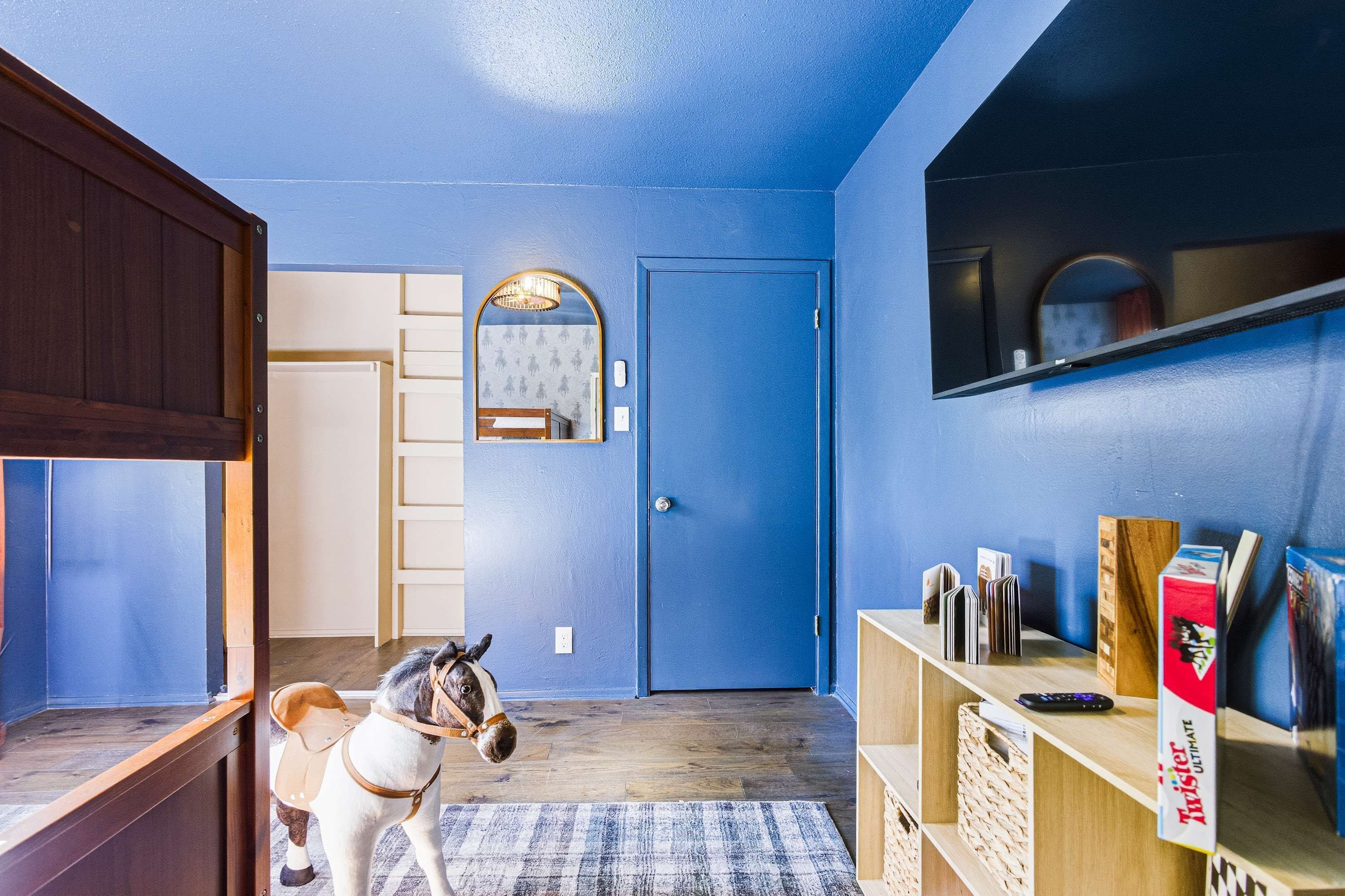 A room with a blue door, a mirror, a horse statue, and a shelf with books and a Twister Ultimate box.