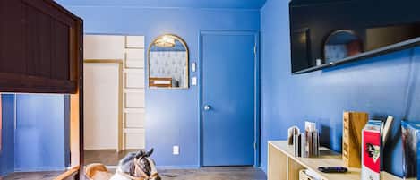Una habitación con puerta azul, un espejo, una estatua de caballo y una estantería con libros y un juego Twister Ultimate.