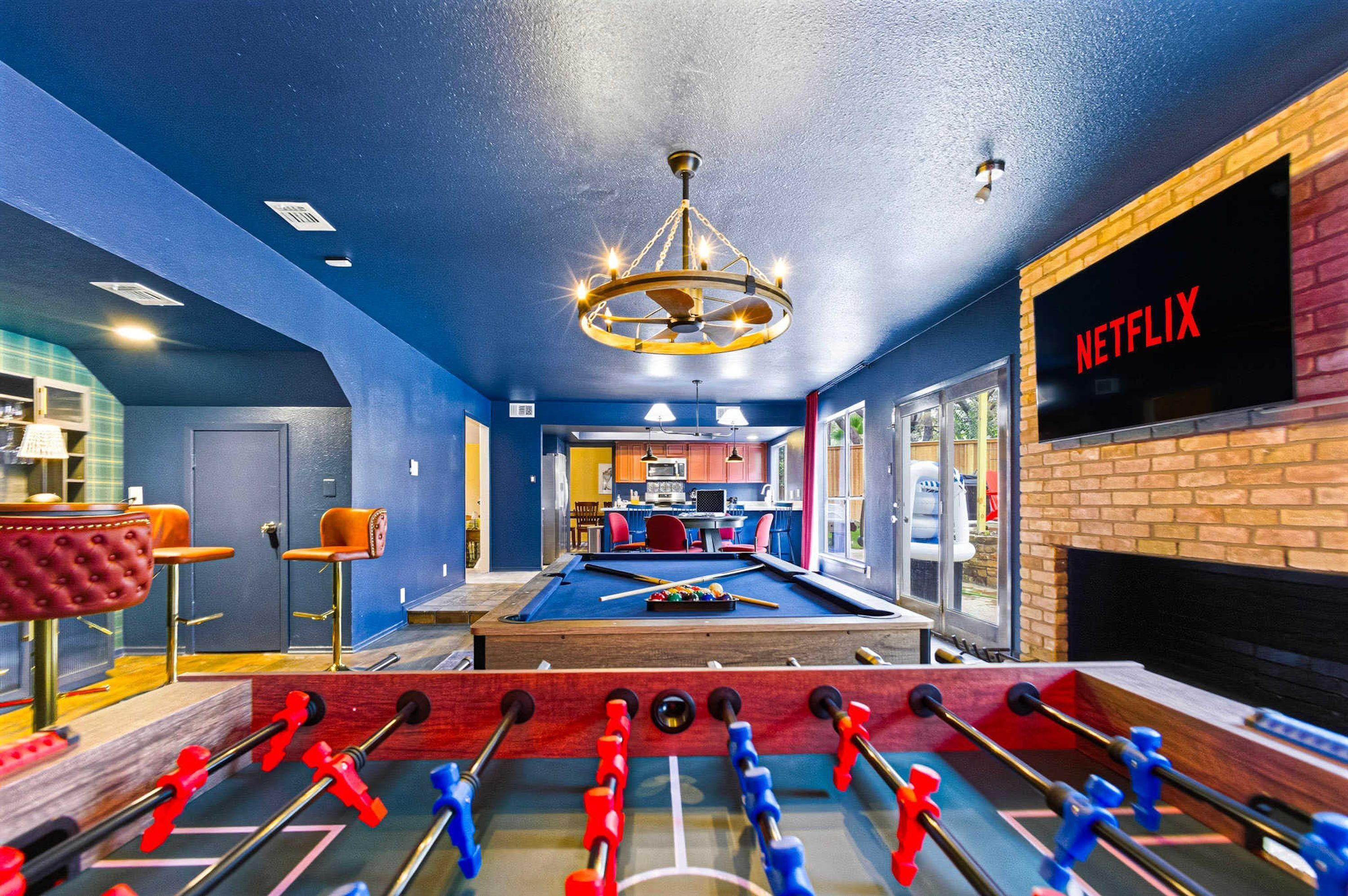 A room with a foosball table, a pool table, and a Netflix sign on the wall.