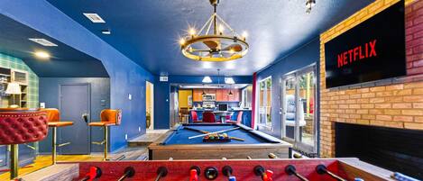 A room with a foosball table, a pool table, and a Netflix sign on the wall.