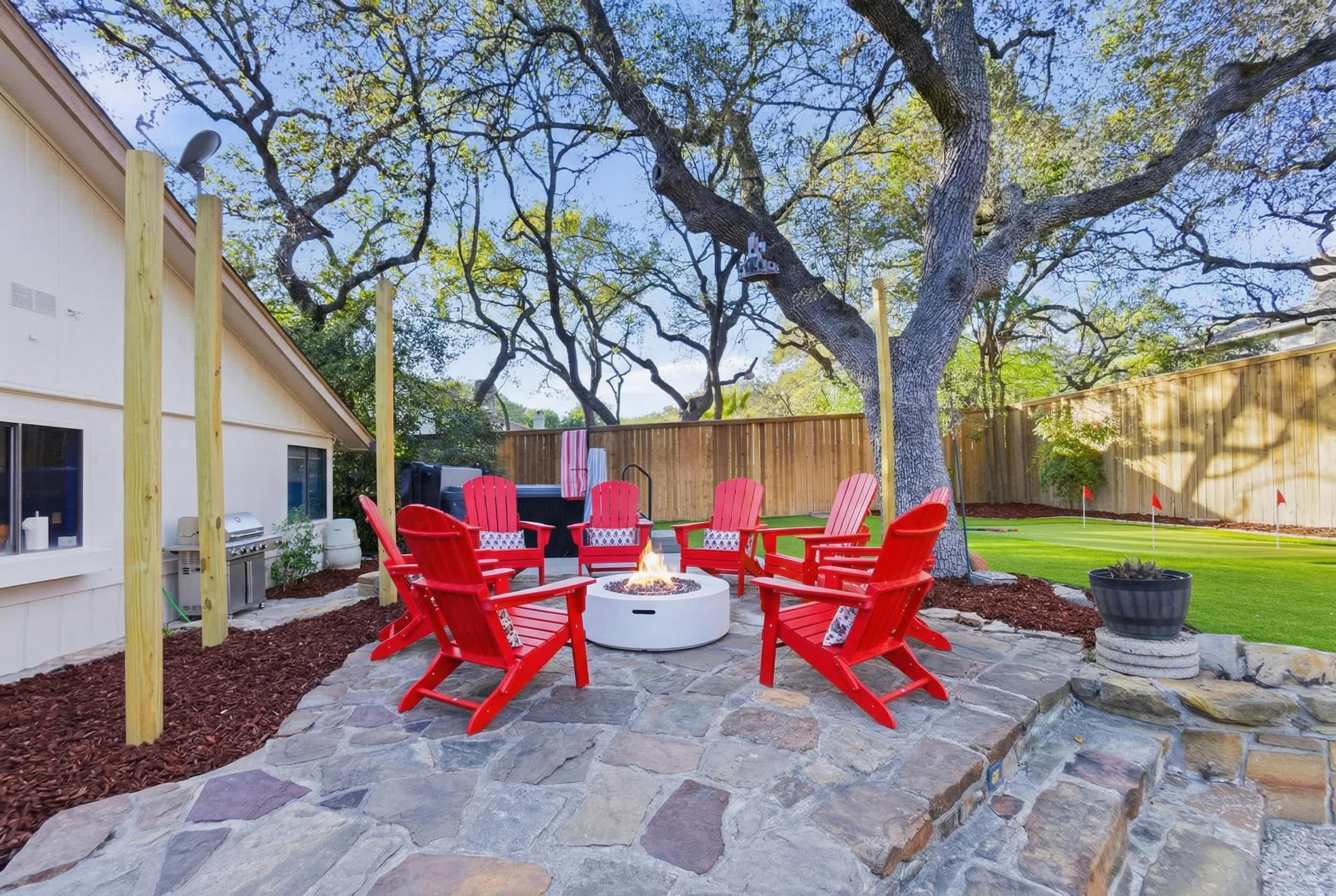 A patio with red Adirondack chairs, a stone fire pit, and a wooden fence.