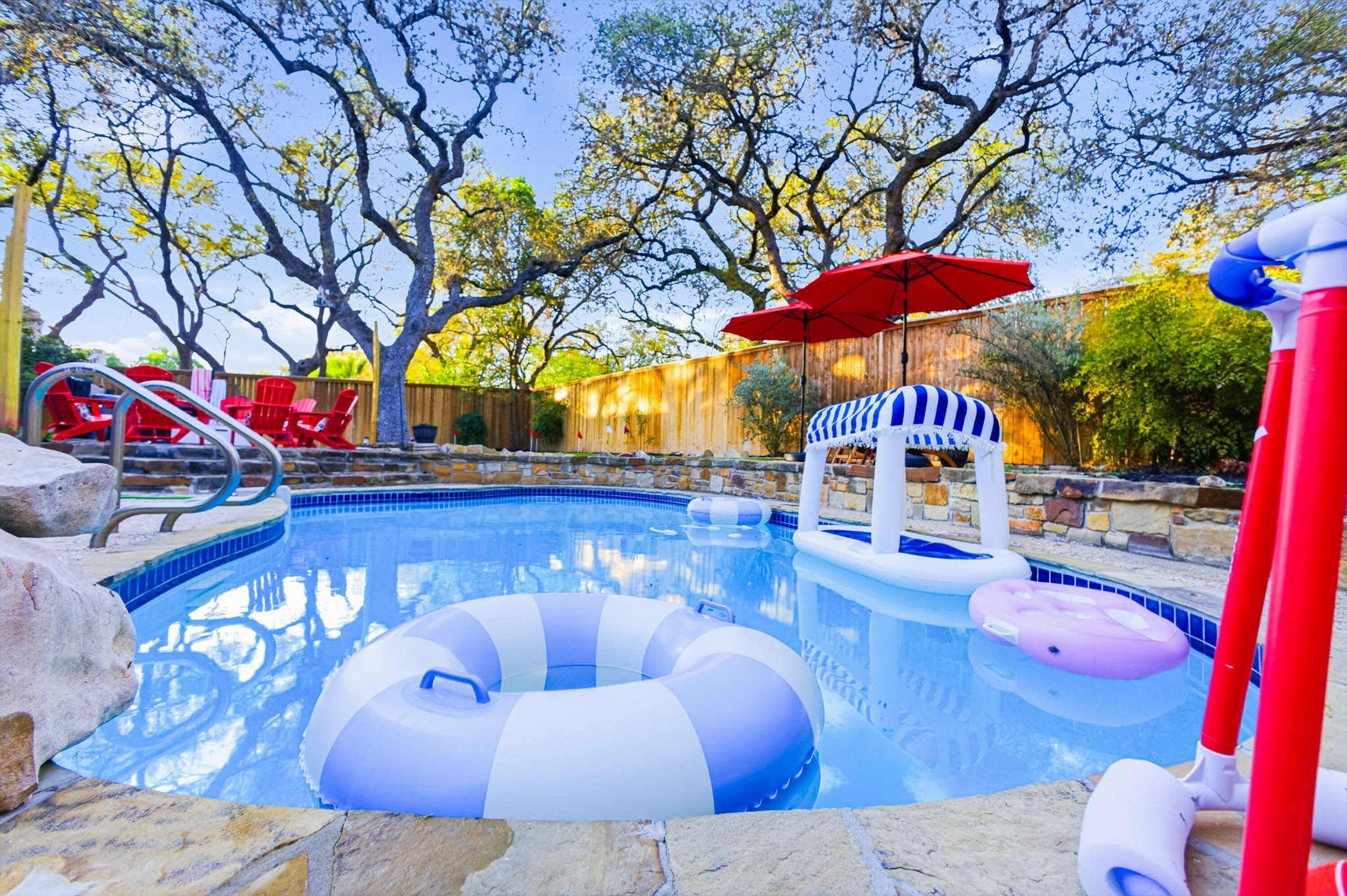 A swimming pool with inflatable rings, a red umbrella, and a wooden fence in the background.