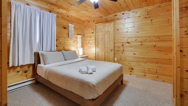 Un dormitorio con paneles de madera, una cama, un ventilador de techo y una ventana con cortinas.