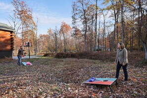 A wooden cabin with a basketball hoop and a table tennis table in a wooded area. - Mountain Retreat Hot Tub Game Room Basketball (Parryville)