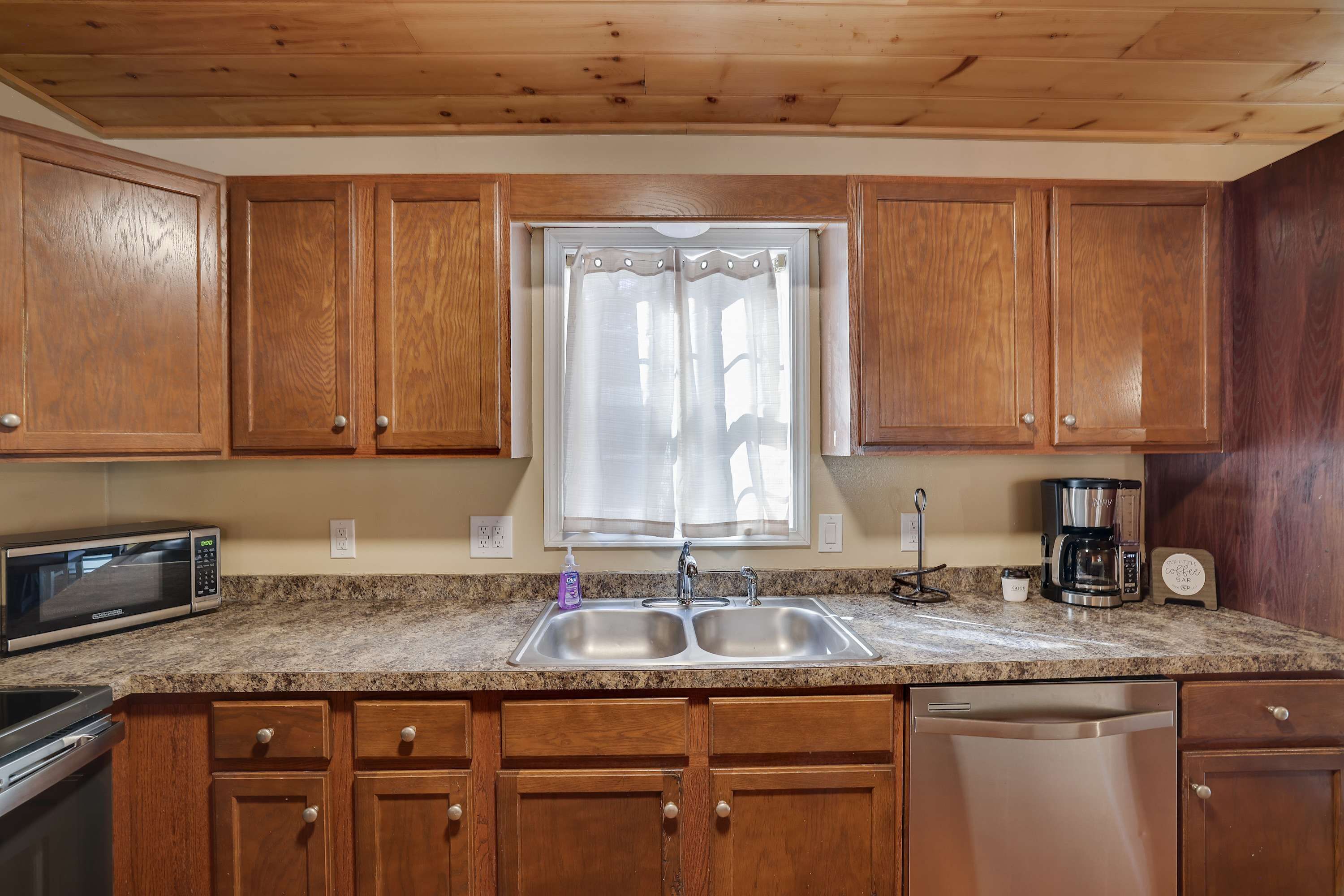 A kitchen with wooden cabinets, a double sink, a microwave, a coffee maker, and a dishwasher.