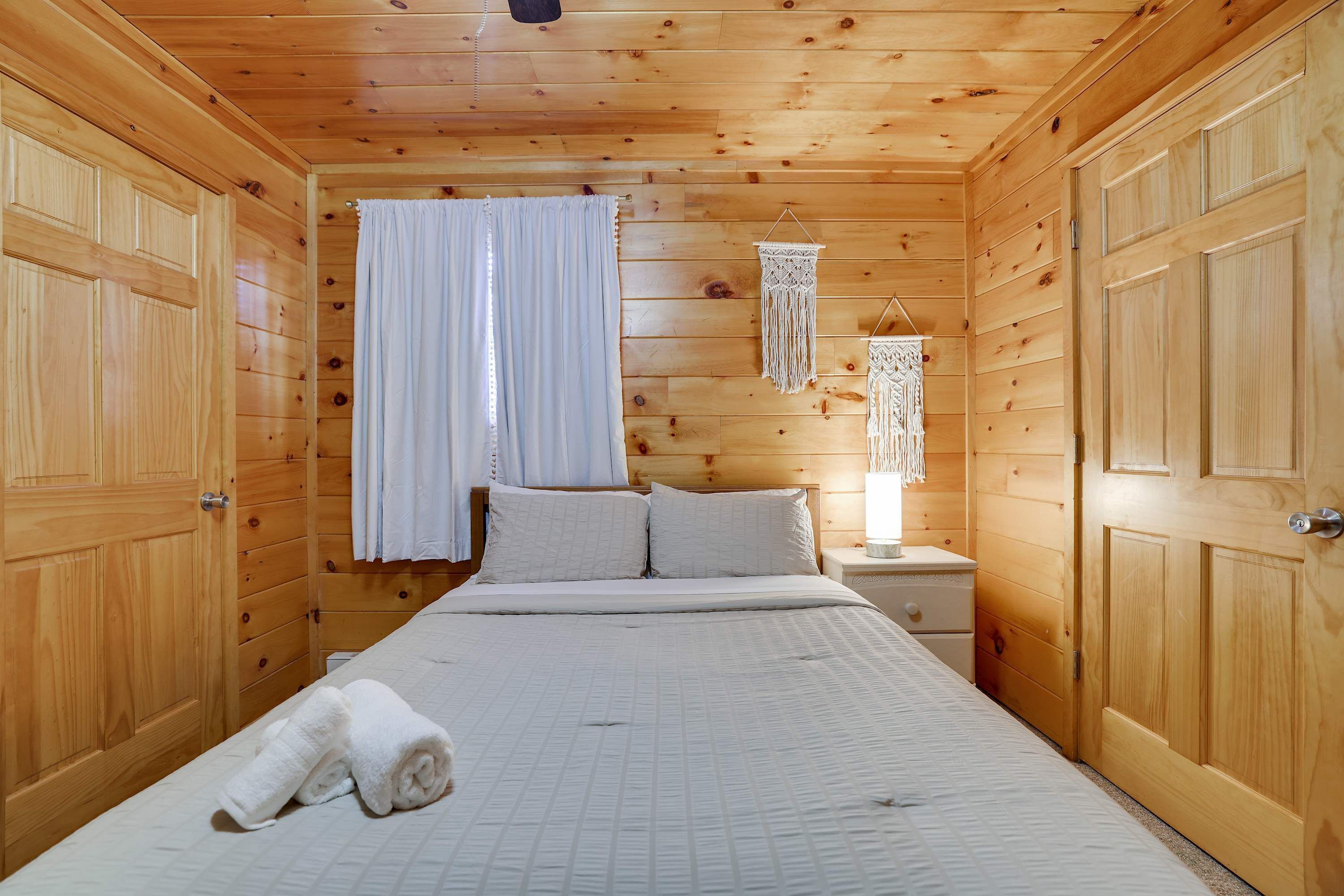A wooden-paneled room with a bed, curtains, a nightstand, and a wall hanging.