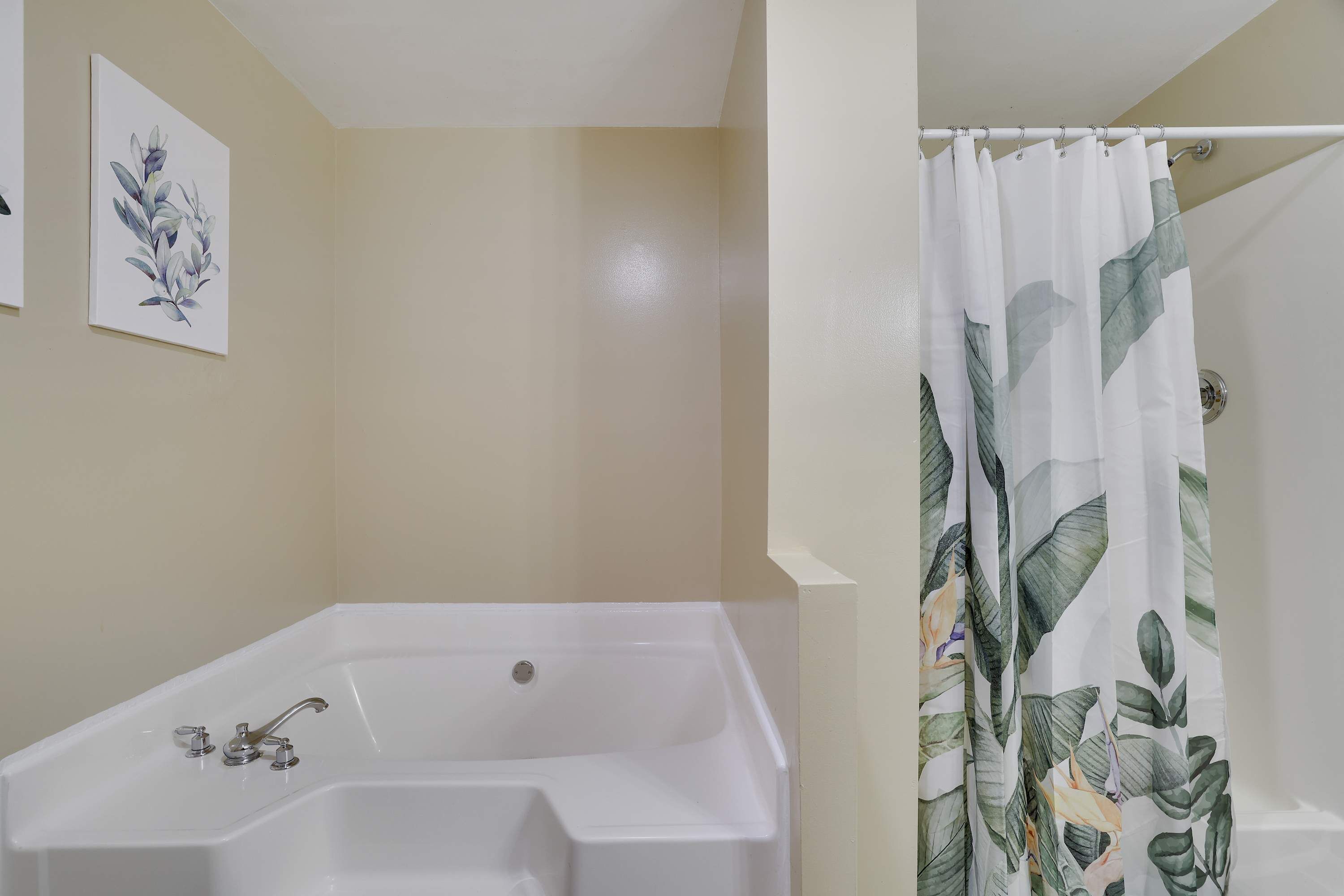 Un baño con bañera, cortina de ducha estampada con hojas y grifo empotrado en la pared.