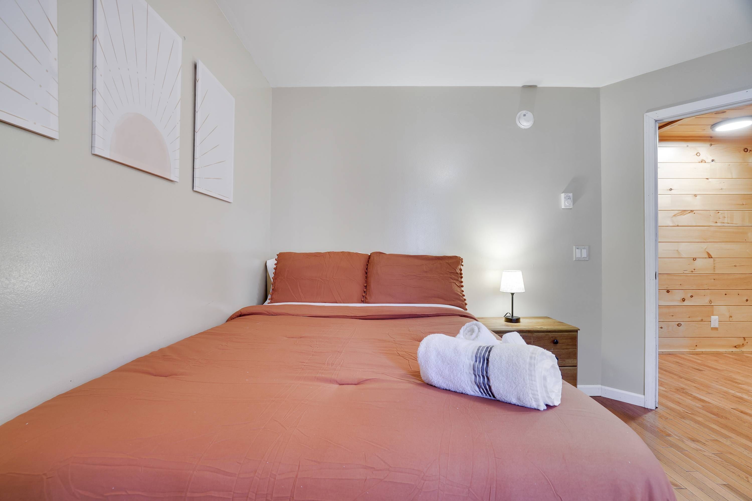 Une chambre à coucher avec un lit, des oreillers, une table de chevet avec une lampe et un plancher en bois.
