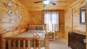 Quarto de cabana de madeira com cama, cômoda e ventilador de teto.