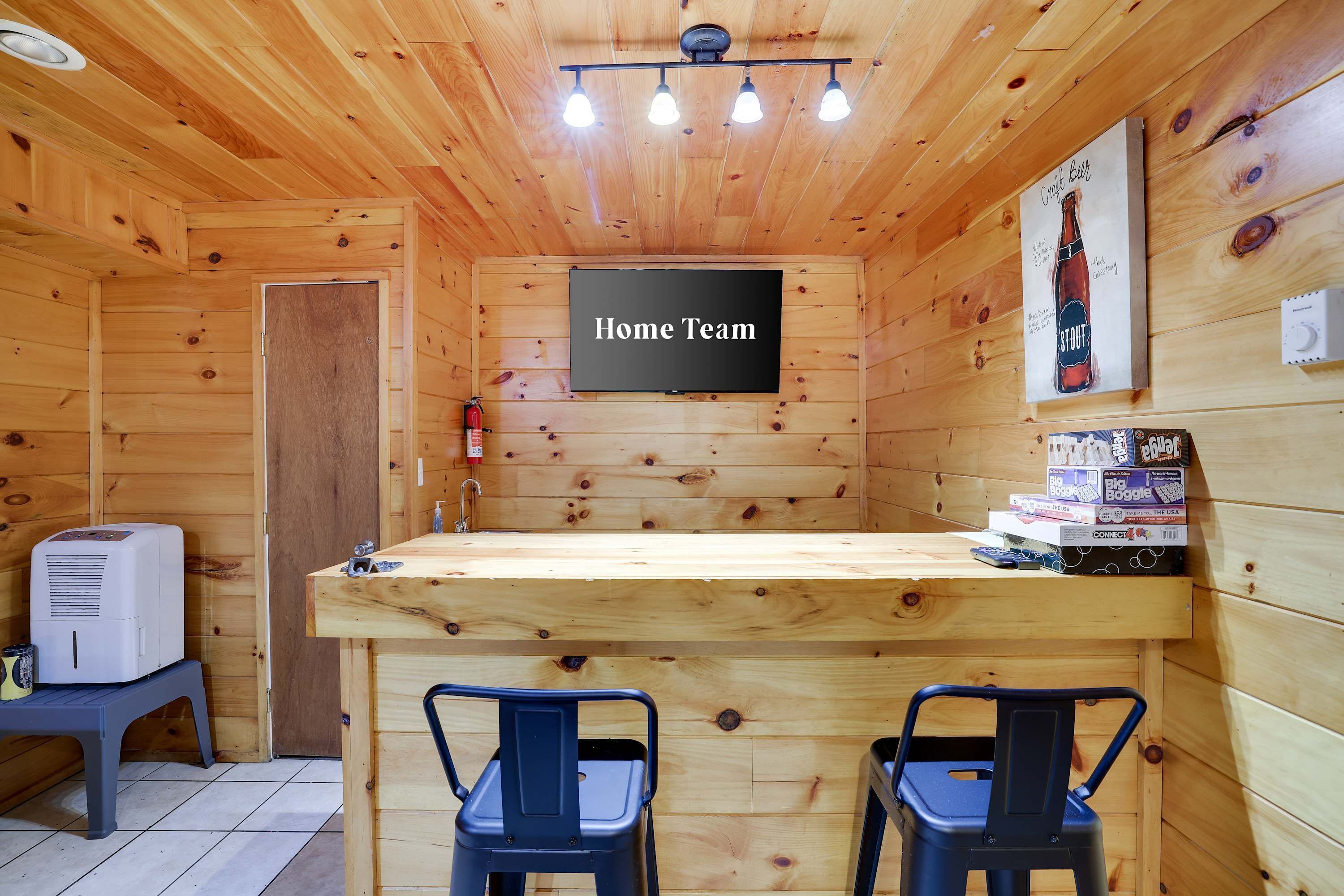 Un interior de madera con una zona de bar, dos sillas, un cartel que dice 'Home Team' y un anuncio de cerveza.