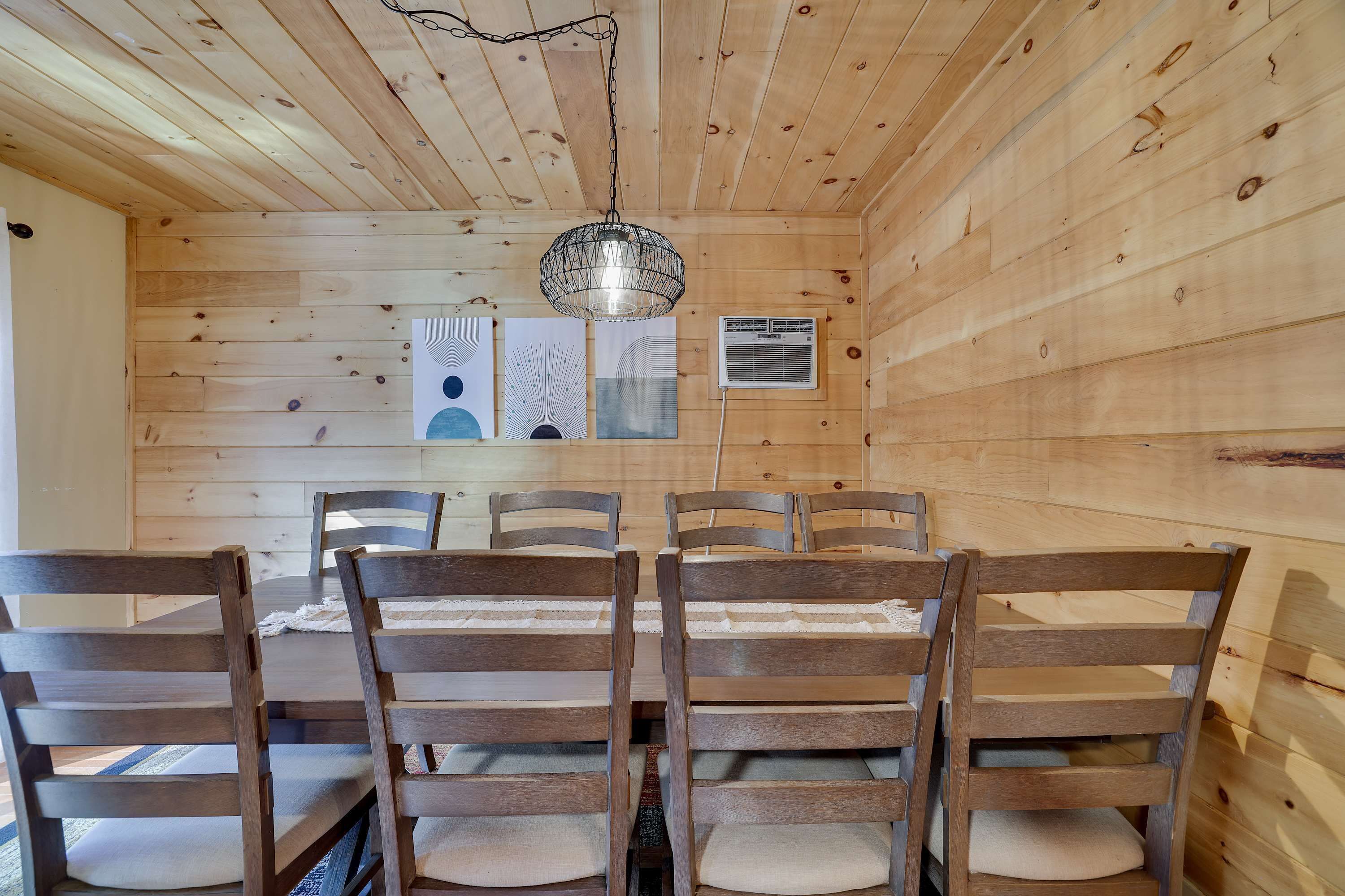 A wooden interior with a dining table and chairs, a hanging light fixture, and a wall-mounted air conditioning unit.
