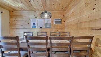 A wooden interior with a dining table and chairs, a hanging light fixture, and a wall-mounted air conditioning unit.
