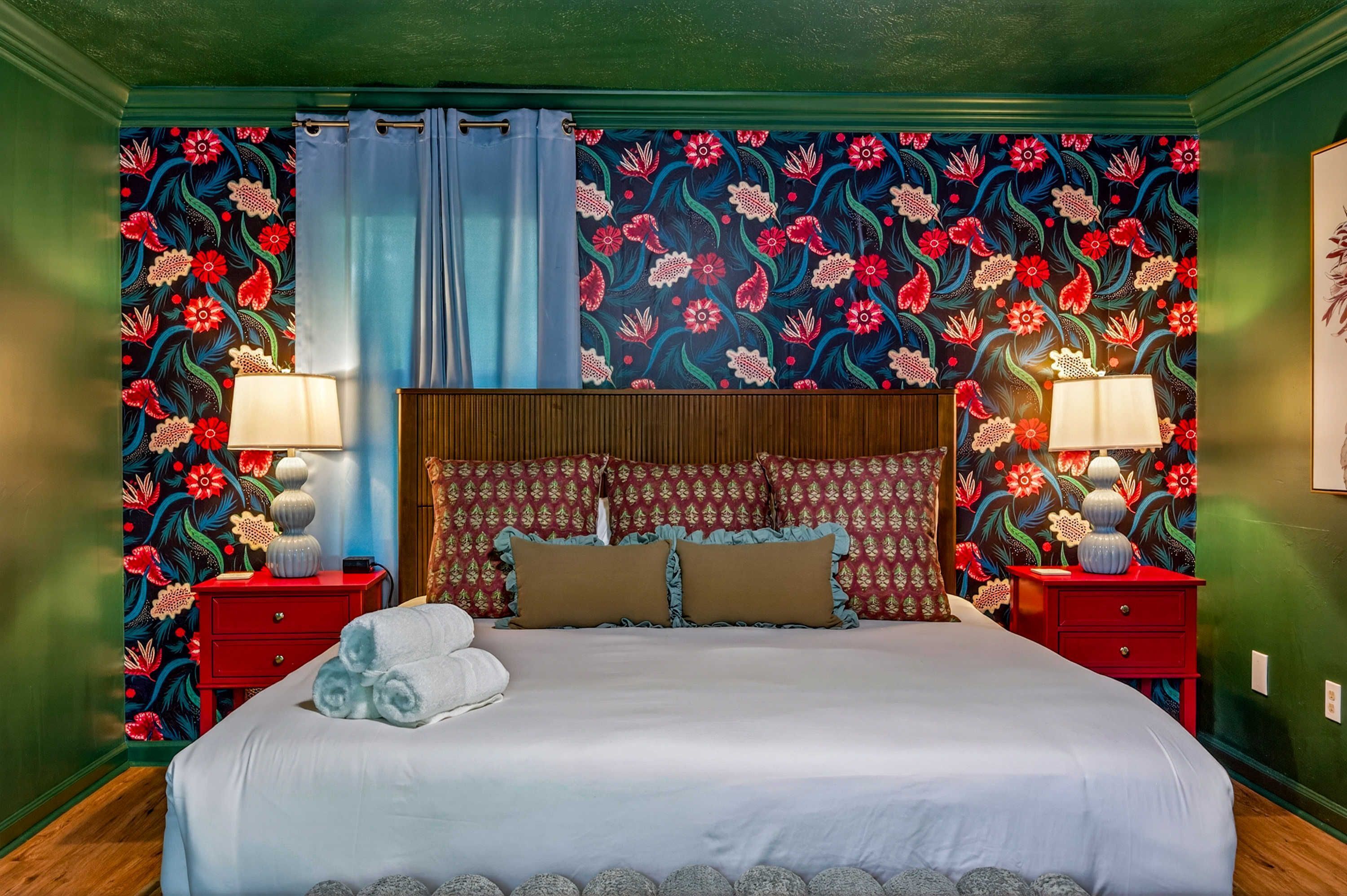 A hotel room with a large bed, two nightstands, a headboard with a floral pattern, and a wall with a floral wallpaper.