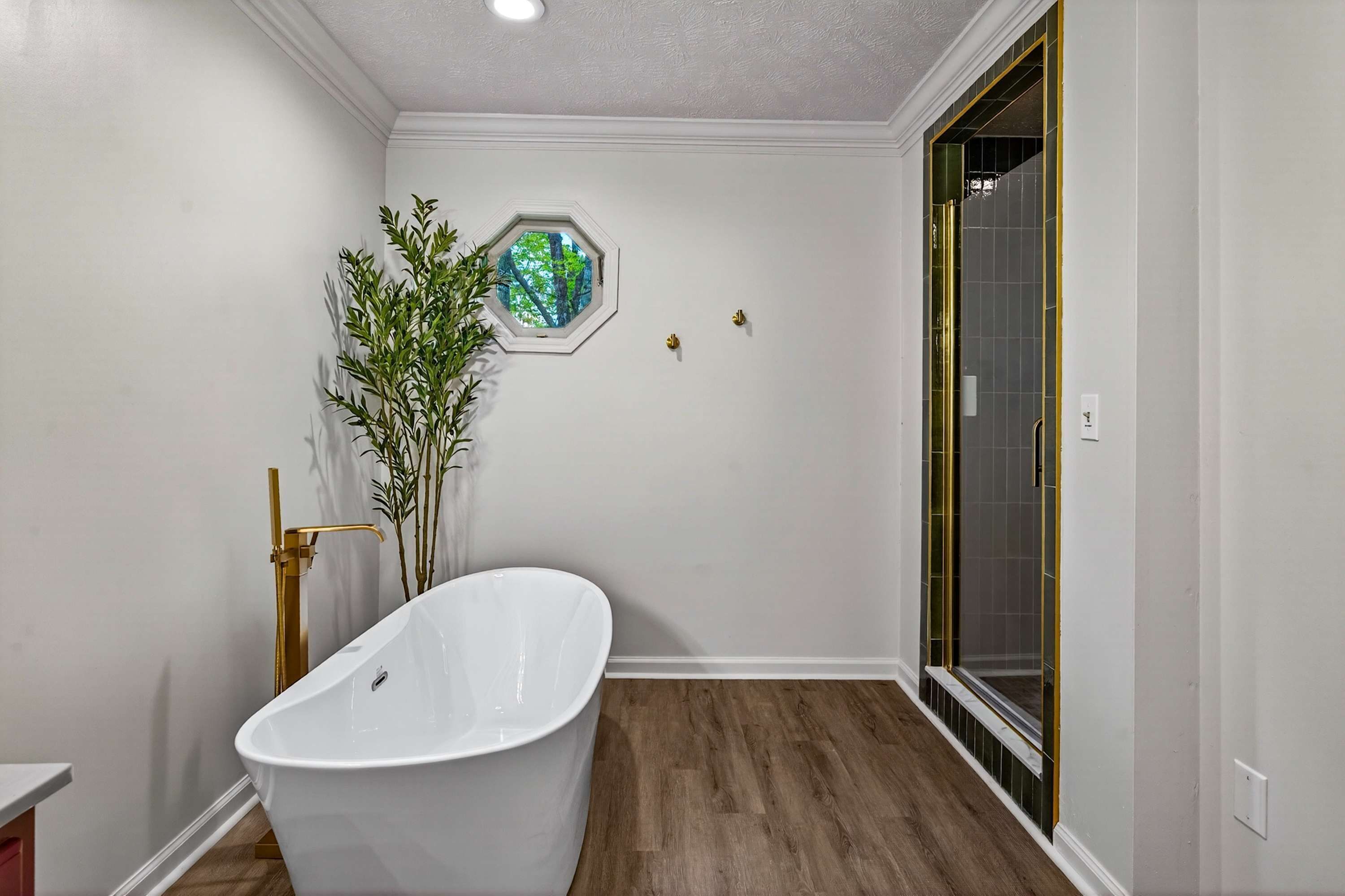Een badkamer met een vrijstaand bad, een douche met glazen deur en een raam met uitzicht op bomen.