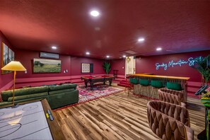 A room with a pool table, green sofas, a neon sign, and a bar area. - Wellsprings Retreat Smoky Mtn Views Sleeps 12 (Gatlinburg)