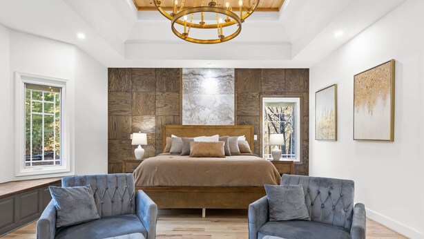 Um quarto com uma cama grande, duas poltronas, um lustre e obras de arte nas paredes.