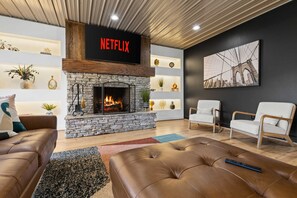 A modern living room with a stone fireplace, leather sofas, and a large wall-mounted TV displaying 'NETFLIX'. - Mtn Views Theater Hot Tub 5 King Suites (Blue Ridge)