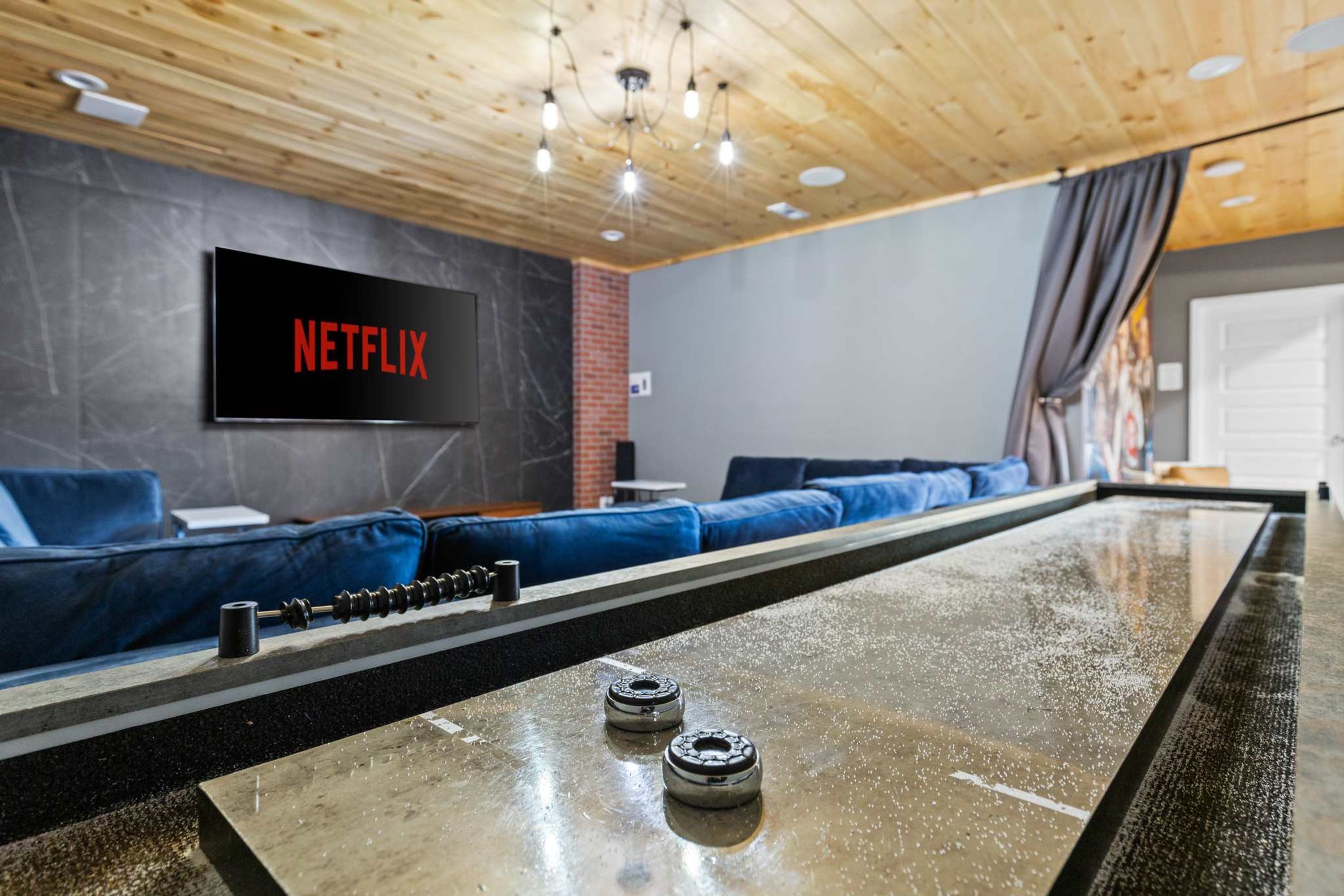A modern lounge area with a Netflix screen, blue seating, and a pool table.