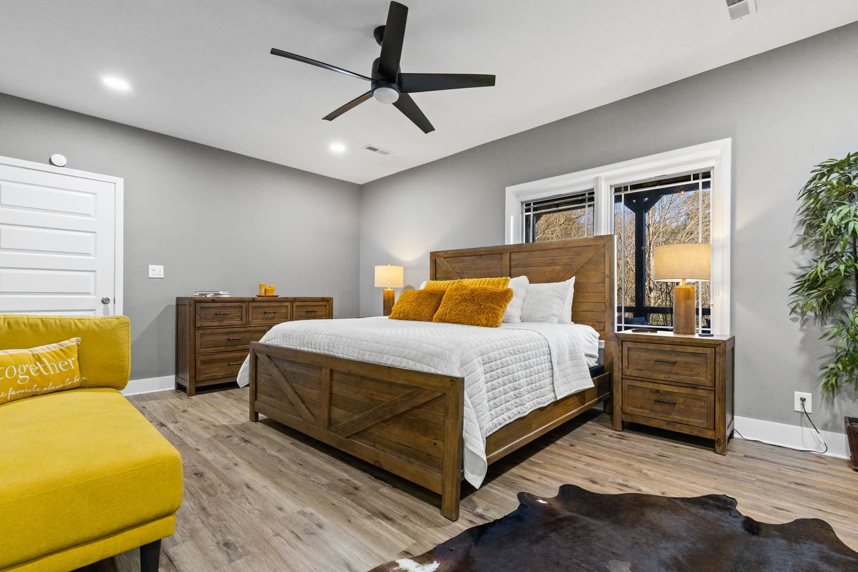 A bedroom with a bed, bedside tables, a ceiling fan, a window with a view, and a yellow armchair.