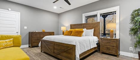 A bedroom with a bed, bedside tables, a ceiling fan, a window with a view, and a yellow armchair.