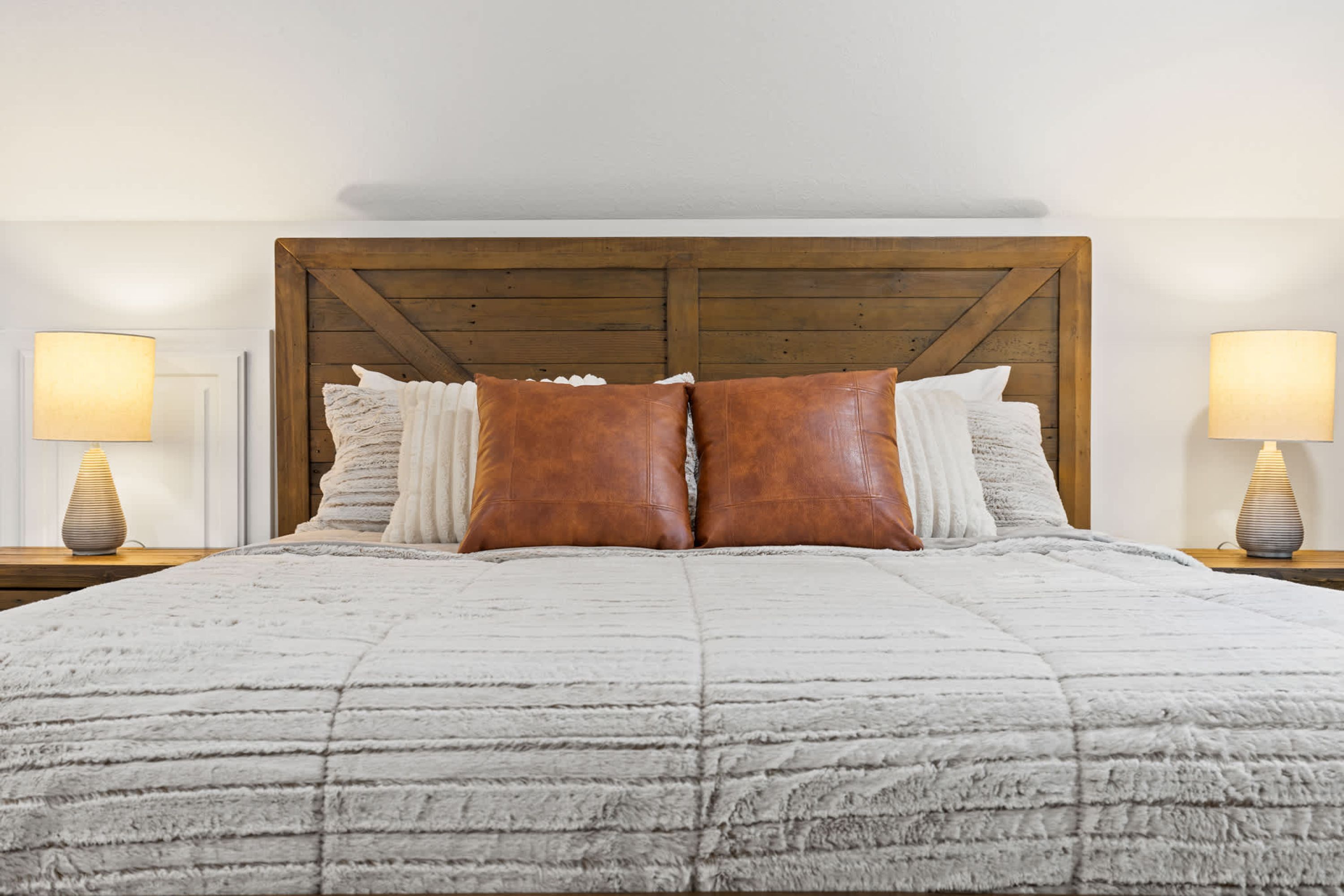 A bed with a wooden headboard, two nightstands with lamps, and multiple pillows.