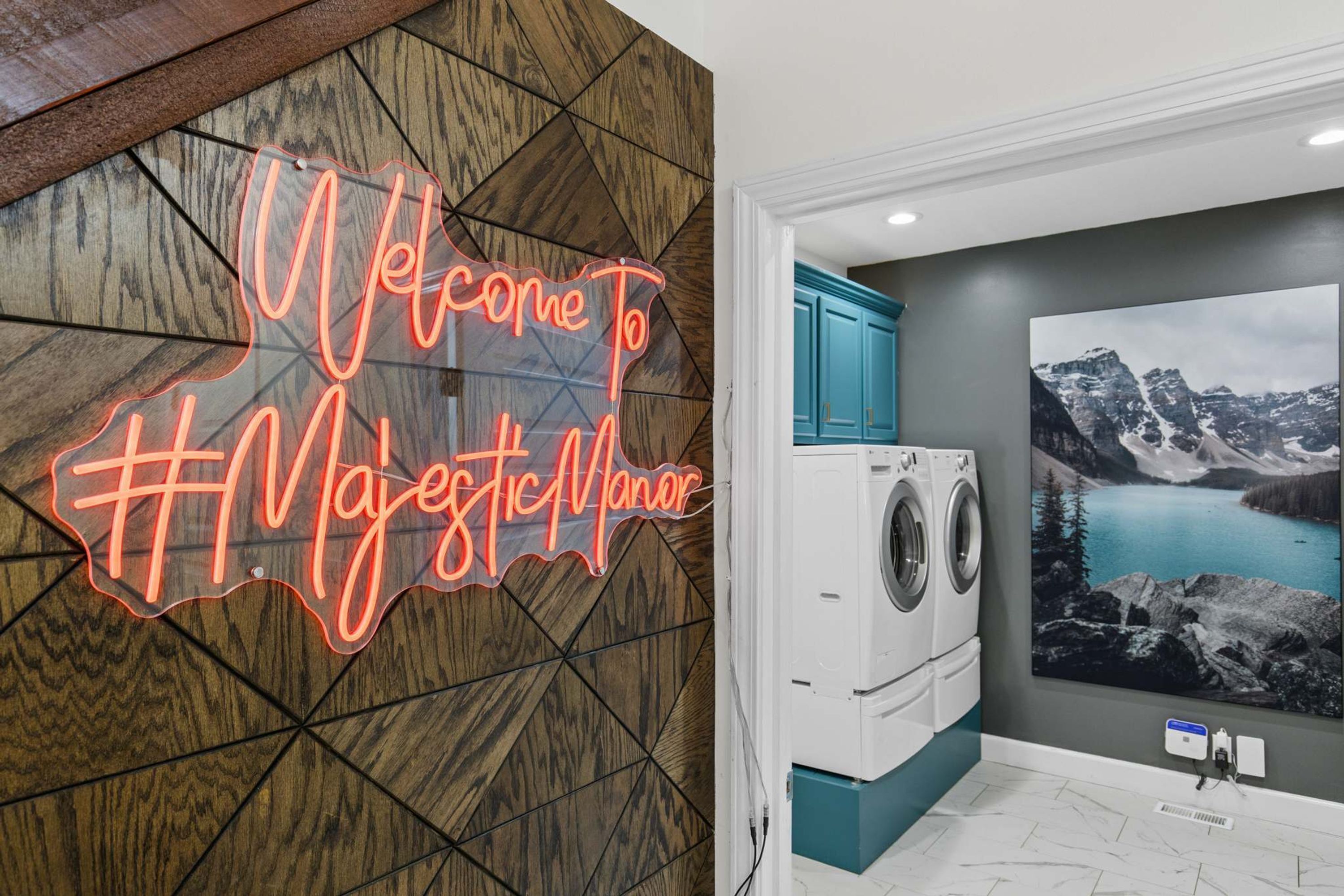A room with a welcome sign, a washing machine, and a mountain landscape painting.