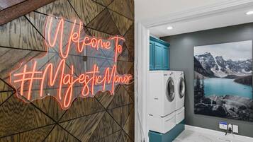 A room with a welcome sign, a washing machine, and a mountain landscape painting.