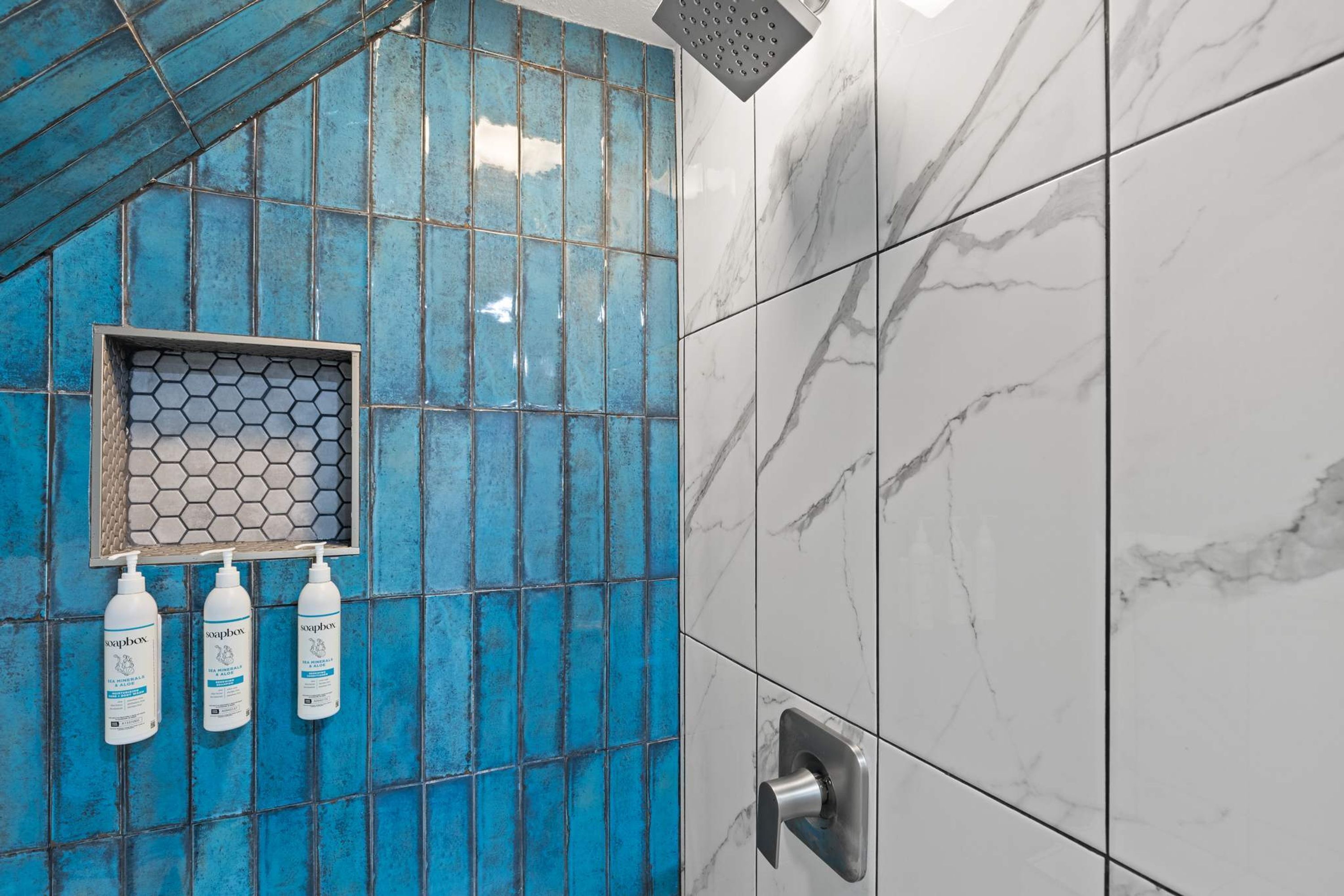 Baño con azulejos azules, un dispensador de jabón hexagonal y un regulador de ducha.