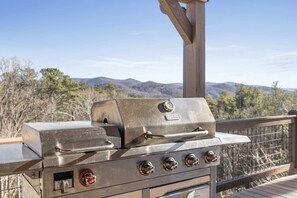 A stainless steel outdoor grill with four burners and a side burner, mounted on a wooden deck with a view of mountains in the background. - Mtn Views Theater Hot Tub 5 King Suites (Blue Ridge)